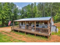 Charming single-story home with a covered front porch and wooden railings, surrounded by lush greenery and an American flag at 6160 Campbellton Redwine Rd, Chattahoochee Hills, GA 30268
