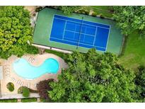 Stunning aerial view showcases a blue tennis court and sparkling pool surrounded by lush green trees at 13 Ivy Ne Sq, Atlanta, GA 30342
