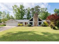 Ranch-style house with a stone chimney, a two-car garage and well-manicured lawn and mature landscaping at 297 Northgate Trce, Roswell, GA 30075