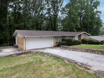 A charming single-story home features a stone accent wall, attached garage and long driveway with a lush, green yard at 4135 Sunrise Trail, Atlanta, GA 30349