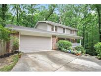 Charming two-story home featuring an attached garage, front porch, brick facade, and lush green landscaping at 3025 Mountain Creek Ne Ct, Roswell, GA 30075