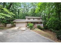 Charming two-story home with a front porch and a spacious driveway surrounded by lush greenery at 3025 Mountain Creek Ne Ct, Roswell, GA 30075