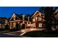 Inviting brick home with a three-car garage and manicured landscaping is beautifully lit in the evening at 1250 Atherton Park, Roswell, GA 30076