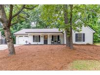 Charming, single-story home with white brick, black shutters, rocking chairs, and manicured landscaping at 2038 Summertown Dr, Norcross, GA 30071