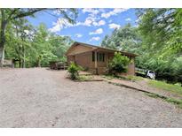 Charming brick home with a covered porch and a spacious gravel driveway, surrounded by lush greenery at 129 Bill Smith Dr, Canton, GA 30114