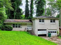 Split-level home with brick facade, lush greenery, attached garage with damaged door and overgrown yard at 3429 Pheasant Ct, Decatur, GA 30034