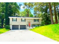 Charming split-level home with a two-car garage, a lush green lawn, and mature trees providing shade at 6965 Kimberland Gardens Ln, Lithonia, GA 30058