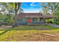 Charming one-story home with a red door, a covered carport, and mature trees on a lush lawn at 1731 Maryland Sw Ave, Marietta, GA 30008