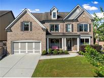 Charming brick home featuring a well-manicured lawn, attached garage, and inviting front porch with seating at 5157 Sunlake Dr, Hoschton, GA 30548