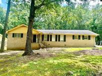 Cozy single-story brick home featuring green lawn and dark shuttered windows nestled among mature trees at 574 Horseshoe Sw Cir, Lilburn, GA 30047