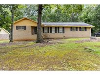 Charming single-story brick home featuring black shutters and mature trees in a lush front yard at 574 Horseshoe Sw Cir, Lilburn, GA 30047