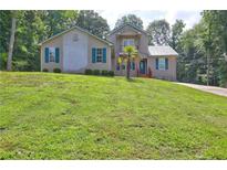 Two-story home with tan siding, teal shutters, a metal roof, and a well-manicured lawn with mature trees at 165 Country Mill Ln, Stockbridge, GA 30281
