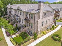 Brick townhome featuring a landscaped yard, a private balcony, and a black iron fence at 134 Everley Walk, Alpharetta, GA 30009