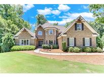 Charming stone home with a well-manicured lawn, mature trees, and beautiful landscaping at 8240 Hurakan Creek Xing, Cumming, GA 30028