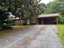 Modest one-story home featuring a brick facade, a large carport, and a driveway at 1932 Pharrs Rd, Snellville, GA 30078