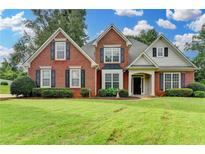 Charming two-story brick home with lush lawn, manicured landscaping, and classic black shutters at 5036 Weatherstone Drive, Buford, GA 30519