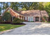 Charming brick home featuring a well-manicured lawn, mature trees, and a circular driveway leading to a double-door entrance at 8900 River Trace Dr, Johns Creek, GA 30097