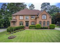 Stately brick home featuring manicured lawn, mature trees, and traditional architectural details at 1952 Sugarstone Dr, Lawrenceville, GA 30043