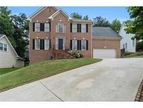 Traditional two-story brick home with a manicured lawn and a long driveway leading to a two-car garage at 2167 Merrymount Dr, Suwanee, GA 30024