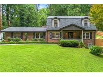 Charming brick home with a well-manicured lawn and lush greenery, showcasing classic architectural details at 1050 Lake Charles Dr, Roswell, GA 30075