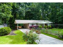 Charming single-story brick home with a covered carport, a well-manicured lawn, and a split rail fence at 514 Macedonia Forest Circle Cir, Canton, GA 30115