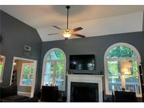 Bright living room featuring a fireplace, ceiling fan, and arched windows overlooking a green outdoor space at 990 Fountain Glen Dr, Lawrenceville, GA 30043