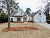 Charming white farmhouse exterior featuring a gable roof, two-car garage and beautifully landscaped front yard at 6149 Pinewood Se Dr, Covington, GA 30014