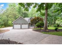 Inviting home featuring a two-car garage and a circular driveway, all surrounded by mature trees and lush landscaping at 1104 Fox Ln, Woodstock, GA 30188
