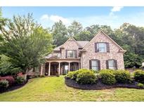 Charming brick home featuring a manicured lawn, dark wood shutters, and a welcoming front porch with stone columns at 208 Grandmar, Canton, GA 30115