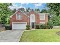 Charming brick home with a well-manicured lawn and a two-car garage, framed by lush trees on a sunny day at 5015 Riverthur Pl, Peachtree Corners, GA 30096