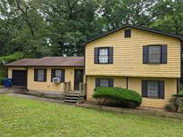 Charming yellow home with dark shutters, a well-manicured lawn, and mature trees in a serene, verdant setting at 234 Park Place Dr, Lawrenceville, GA 30046