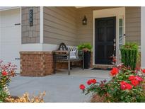Inviting front porch with a black door, brick accents, a bench, and vibrant red roses at 4583 Grenadine Cir, Acworth, GA 30101