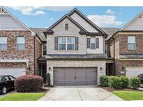 Charming brick townhome featuring a two-car garage, manicured lawn, and classic architectural details at 8215 Harlond Way, Suwanee, GA 30024