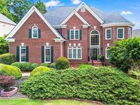 Charming red brick home featuring lush landscaping, black shutters, and a beautiful round turret on the right side at 1000 Gunter Ct, Alpharetta, GA 30022
