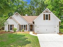 Charming, traditional-style white home with brown shutters, a well-manicured lawn, and mature trees in the background at 4210 Platinum Ct, Hoschton, GA 30548