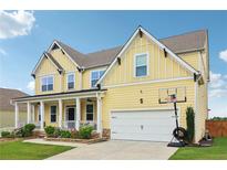 Two-story yellow home with a covered porch, lush landscaping, and an attached two-car garage at 1564 Brunswick St, Lithia Springs, GA 30122