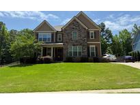 Charming two-story home boasts a stone and siding facade, complemented by a lush green lawn and well-manicured landscaping at 8340 Nolandwood Ln, Villa Rica, GA 30180