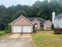 Charming brick home featuring a two-car garage and a well-maintained front lawn and lush green trees at 7513 Sugarcreek Dr, Riverdale, GA 30296