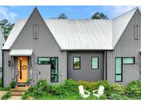 Charming home featuring a metal roof, gray vertical siding, an orange door and inviting front lawn with two white chairs at 10862 Serenbe Ln, Chattahoochee Hills, GA 30268