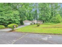 Ranch-style home with a well-manicured lawn and driveway leading to an attached garage, surrounded by mature trees at 5577 Whittondale Rd, Lithonia, GA 30058