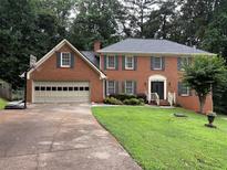 Charming two-story red brick home featuring an attached garage, well-manicured lawn, and lush trees at 2181 Rodao Sw Dr, Lilburn, GA 30047
