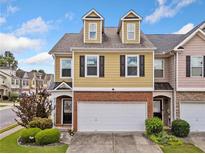 Charming townhome featuring yellow siding, dormer windows, a brick foundation, and a two-car garage at 44 Providence Oak Ct, Lawrenceville, GA 30046