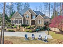 Inviting stone and brick home featuring a landscaped front yard with a multi-car driveway and beautiful trees at 11180 West Rd, Roswell, GA 30075