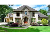 Elegant home featuring a manicured lawn, stone accents, and a welcoming arched entryway with a wood door at 2910 Creek Tree Ln, Cumming, GA 30041