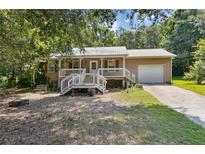 Charming ranch-style home with a metal roof, front porch, and attached garage, nestled amongst lush greenery at 136 Pine St, Covington, GA 30014