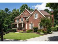 Traditional two-story red brick home with manicured lawn and inviting front porch in a tree-lined neighborhood at 200 Long Needle Ct, Sugar Hill, GA 30518