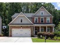 Charming two-story home featuring a two-car garage, stone accents, and a well-maintained front yard with mature trees at 6695 Grove Meadows Ln, Cumming, GA 30028