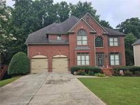 Traditional two-story brick home with a two-car garage, manicured lawn, and mature trees at 3930 Regal Oaks Dr, Suwanee, GA 30024
