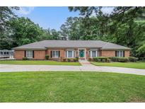 Charming single-story brick home with a green lawn, large driveway, and lush, mature trees at 3003 Hanover Se Ln, Conyers, GA 30094