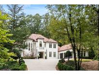 Elegant two-story home with a red tile roof, white exterior and lush landscaping in a wooded setting at 3401 Stillhouse Se Rd, Atlanta, GA 30339